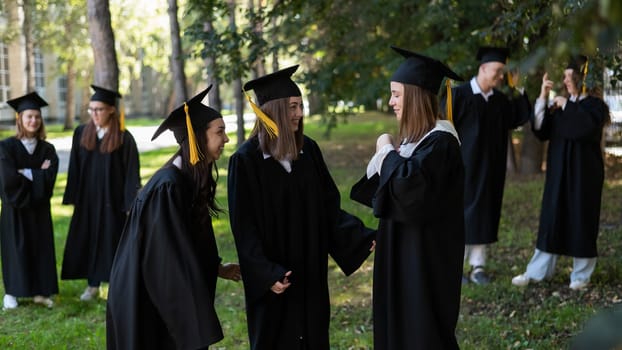 A group of graduates in robes congratulate each other on their graduation outdoors