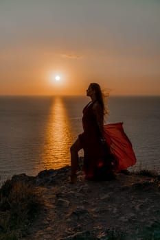 Woman sunset sea red dress, back view a happy beautiful sensual woman in a red long dress posing on a rock high above the sea on sunset