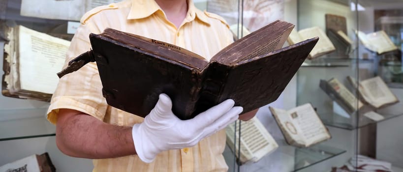 An old book in a scientist's hands, close-up. Christian antique book in the hands of a librarian.