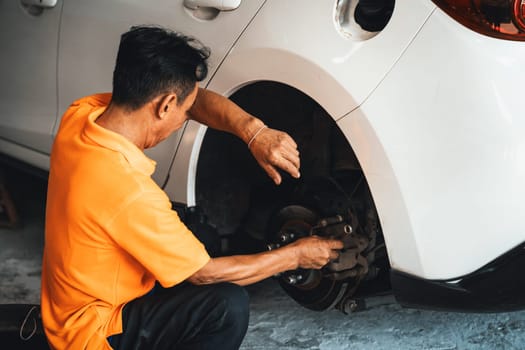 Hardworking mechanic changing car wheel in auto repair workshop. Automotive service worker changing leaking rubber tire in concept of professional car care and maintenance. Oxus
