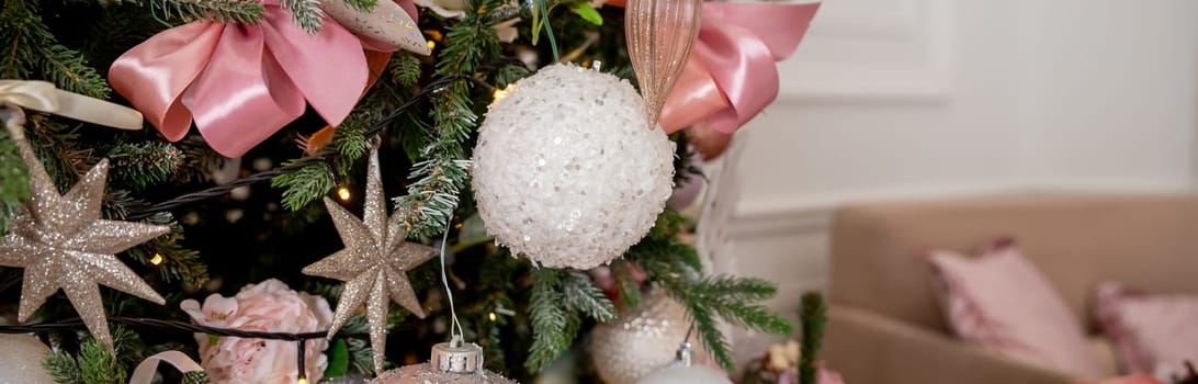 Festive Christmas background, card. Gold Christmas garland, pink Christmas tree decorations and white artificial fir tree on a pink background.