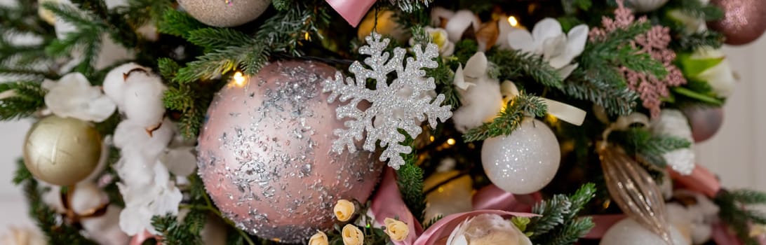 Festive Christmas background, card. Gold Christmas garland, pink Christmas tree decorations and white artificial fir tree on a pink background.