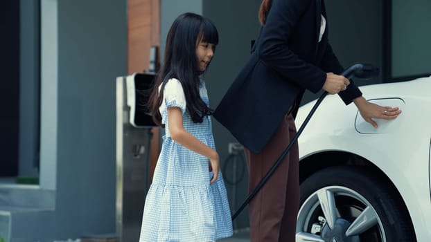 Progressive lifestyle of mother and daughter who have just returned from school in an electric vehicle that is being charged at home. Electric vehicle powered by sustainable clean energy.