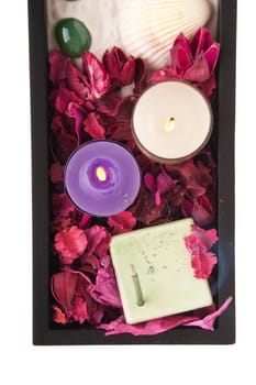 gorgeous spa setting with candles, stones, sand, incense, seashell and dry petal roses and other flowers on a black tray (close-up picture isolated on white background)