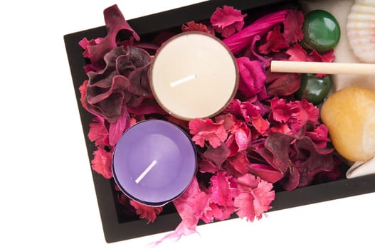 gorgeous spa setting with candles, stones, sand, seashells, rake, dry petal roses and other flowers on a black tray (close up picture isolated on white background)