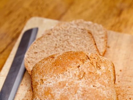 Slices of home made wheat bread on breadboard with knife