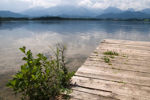 Wide-angle view of wooden jetty with small green bush at Hopfensee in the Allgäu / Bavaria