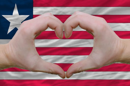 Gesture made by hands showing symbol of heart and love over liberia flag