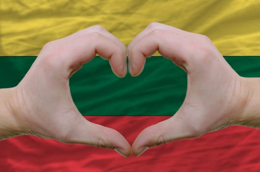 Gesture made by hands showing symbol of heart and love over lithuania flag
