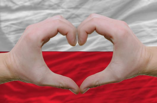 Gesture made by hands showing symbol of heart and love over poland flag