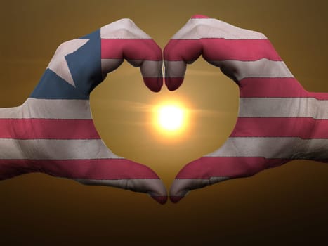 Gesture made by liberia flag colored hands showing symbol of heart and love during sunrise