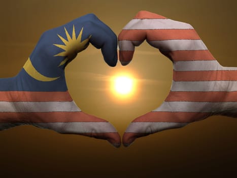 Gesture made by malaysia flag colored hands showing symbol of heart and love during sunrise