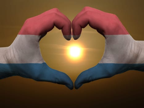 Gesture made by holland flag colored hands showing symbol of heart and love during sunrise