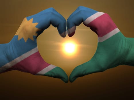 Gesture made by namibia flag colored hands showing symbol of heart and love during sunrise