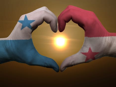 Gesture made by panama flag colored hands showing symbol of heart and love during sunrise