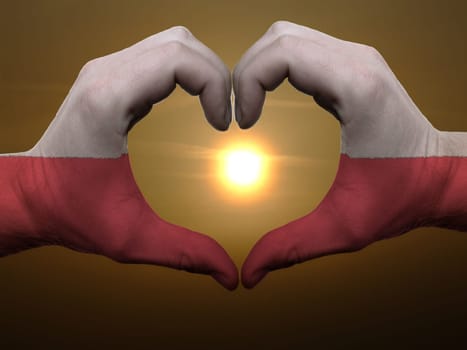 Gesture made by poland flag colored hands showing symbol of heart and love during sunrise