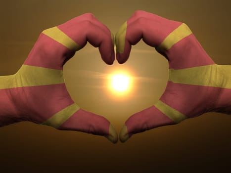 Gesture made by macedonia flag colored hands showing symbol of heart and love during sunrise