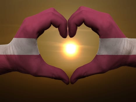 Gesture made by latvia flag colored hands showing symbol of heart and love during sunrise