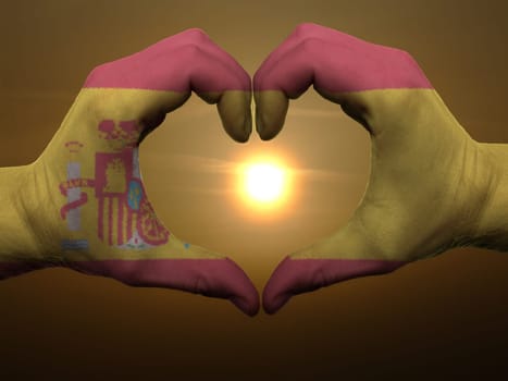 Gesture made by spain flag colored hands showing symbol of heart and love during sunrise
