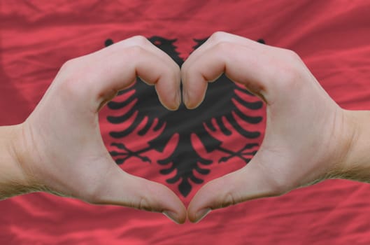 Gesture made by hands showing symbol of heart and love over Albanian flag