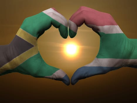 Gesture made by south africa flag colored hands showing symbol of heart and love during sunrise