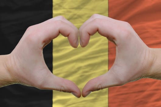 Gesture made by hands showing symbol of heart and love over belgium flag
