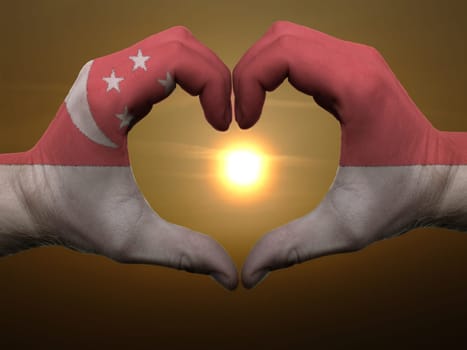 Gesture made by singapore flag colored hands showing symbol of heart and love during sunrise
