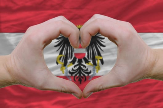 Gesture made by hands showing symbol of heart and love over austrian flag