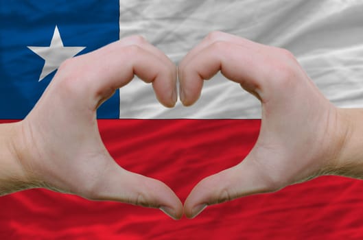 Gesture made by hands showing symbol of heart and love over chile flag