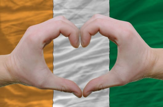 Gesture made by hands showing symbol of heart and love over ivory coast flag