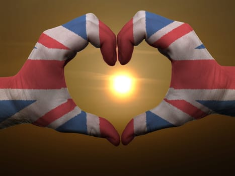 Gesture made by united kingdom flag colored hands showing symbol of heart and love during sunrise