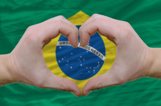 Gesture made by hands showing symbol of heart and love over brazil flag