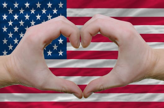 Gesture made by hands showing symbol of heart and love over american flag