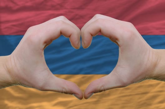 Gesture made by hands showing symbol of heart and love over armenian flag