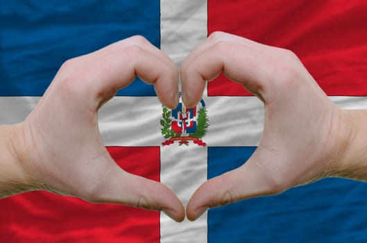 Gesture made by hands showing symbol of heart and love over dominican flag