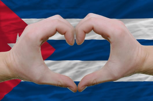 Gesture made by hands showing symbol of heart and love over cuba flag
