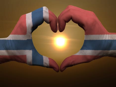 Gesture made by norway flag colored hands showing symbol of heart and love during sunrise