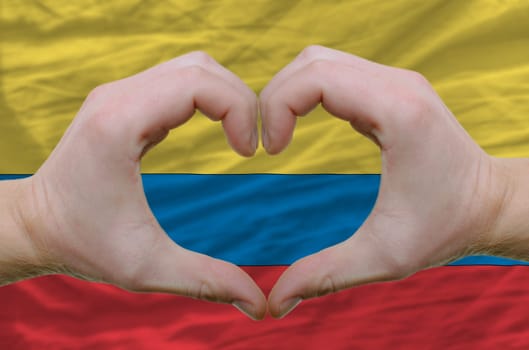 Gesture made by hands showing symbol of heart and love over columbia flag