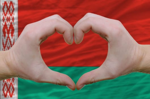 Gesture made by hands showing symbol of heart and love over belarus flag