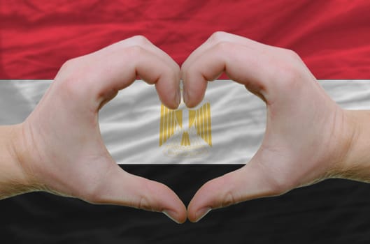 Gesture made by hands showing symbol of heart and love over egypt flag