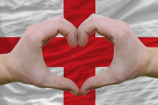 Gesture made by hands showing symbol of heart and love over englandr flag