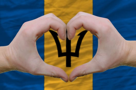 Gesture made by hands showing symbol of heart and love over barbados flag