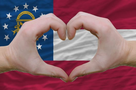 Gesture made by hands showing symbol of heart and love over georgia flag