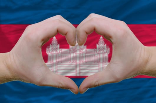 Gesture made by hands showing symbol of heart and love over cambodia flag