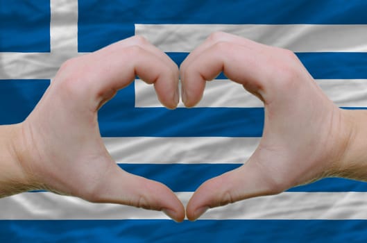 Gesture made by hands showing symbol of heart and love over greece flag