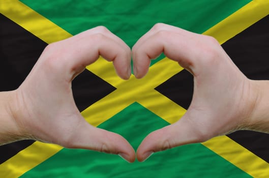 Gesture made by hands showing symbol of heart and love over jamaica flag