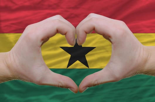 Gesture made by hands showing symbol of heart and love over ghana flag