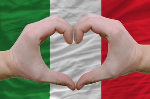 Gesture made by hands showing symbol of heart and love over italy flag