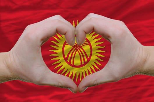 Gesture made by hands showing symbol of heart and love over kyrghyzstan flag