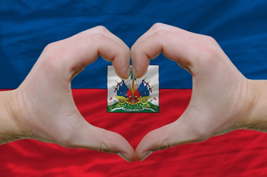 Gesture made by hands showing symbol of heart and love over haiti flag